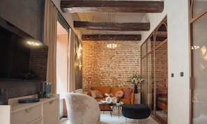 Una habitación acogedora con paredes de ladrillo visto, un televisor grande, un sofá y una mesita con un florero.