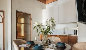 Un comedor con una mesa dispuesta para cuatro, un florero con flores blancas y una cocina al fondo.