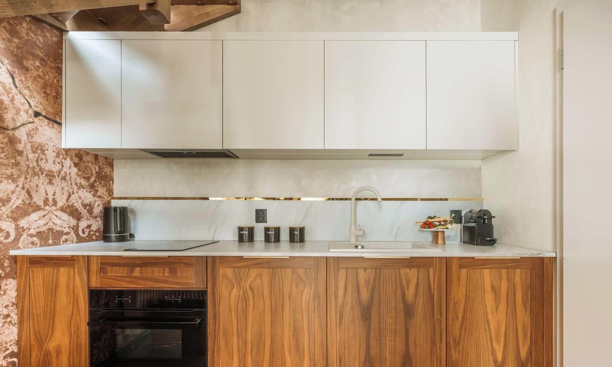 Cocina moderna con armarios de madera, horno empotrado, cafetera y un lavamanos.