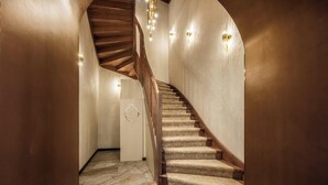 Eine Wendeltreppe mit Teppichstufen und Holzwertungen, die zu einer Zwischenebene mit einer Wandleuchte führt.