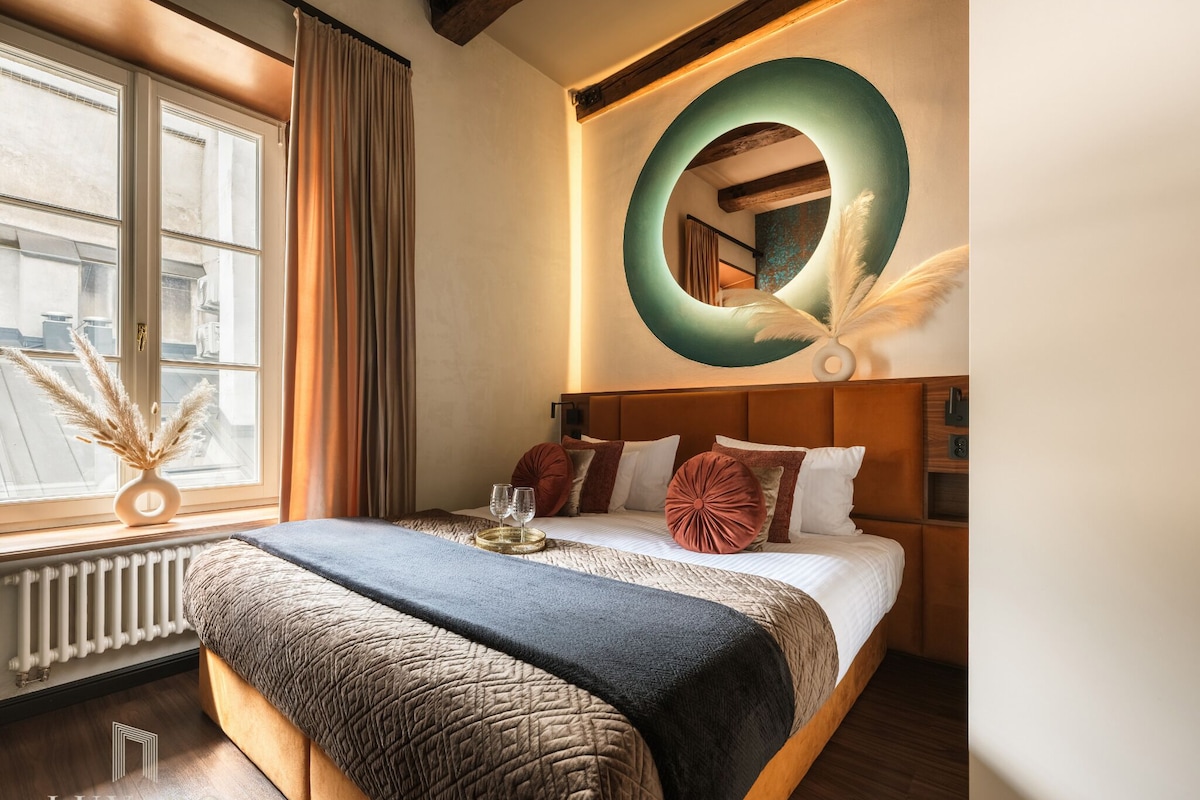 Una habitación de hotel con una cama grande, un espejo redondo y vistas a la ciudad a través de una ventana.