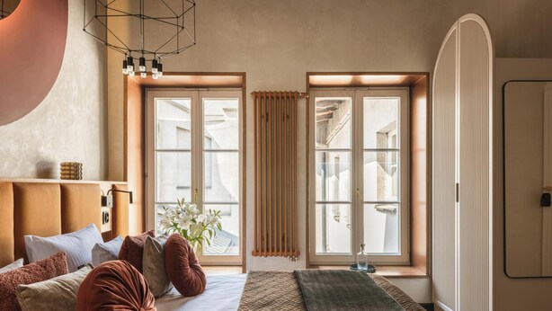 Ein Schlafzimmer mit Bett, Kissen, einem Nachttisch, einem Fenster mit Vorhängen und einer Heizung.