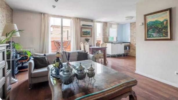 A living room with a sofa, a coffee table with decorative items, a dining area with a table and chairs, and a kitchen in the background. - Stylish Duplex Penthouse with Private Terraces in Ciudad Lineal (Madrid)