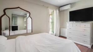 A bedroom with a large bed, a dresser, a television, and a mirror. - Stylish Duplex Penthouse with Private Terraces in Ciudad Lineal (Madrid)