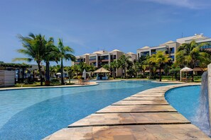 A resort pool with a stone deck, surrounded by palm trees and modern buildings. - Wai Wai #a302 - Beachfront Resort by Carpediem (Caucaia)