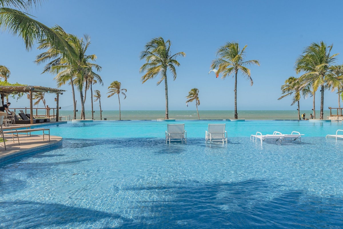 Una piscina blu cristallina con lettini, palme e vista sull'oceano.