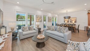 A spacious living room with two sofas, a coffee table, and a dining area with chairs and a table. - Tango! Beach House for 26 Guests! Plus Golf Cart! (Santa Rosa Beach)