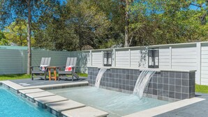A swimming pool with a waterfall feature, lounge chairs, and a small table. - Tango! Beach House for 26 Guests! Plus Golf Cart! (Santa Rosa Beach)