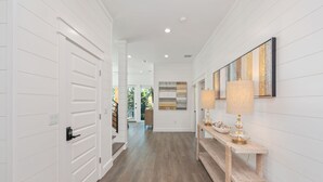 A hallway with white paneled walls, a wooden floor, a console table with a lamp, and a framed artwork on the wall. - Tango! Beach House for 26 Guests! Plus Golf Cart! (Santa Rosa Beach)