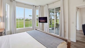 Een slaapkamer met een bed, een plafondventilator, een televisie en grote ramen.