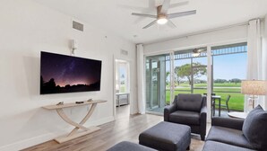 Een moderne woonkamer met een flatscreen televisie, grijze banken, een houten salontafel en een plafondventilator.