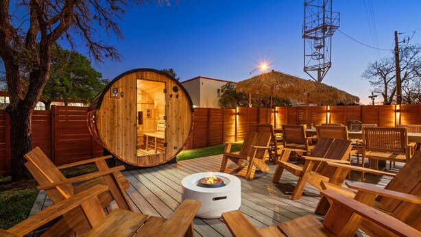 Een houten terras met lounge stoelen en een ronde houten constructie met een deur, omgeven door een houten hek.