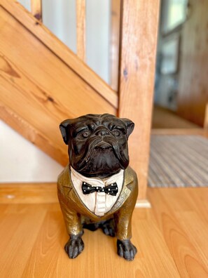 Eine Bulldoggenfigur in Smoking, sitzend auf einem Holzboden.