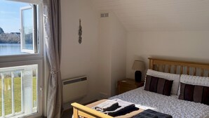 Ein Schlafzimmer mit einem hölzernen Bett, einem Fenster mit Vorhängen, einer Heizung und Blick auf einen See.