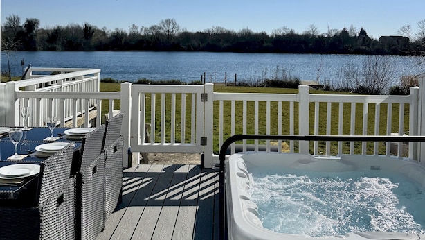 Eine Terrasse mit Whirlpool, weißen Geländern und Blick auf einen See.