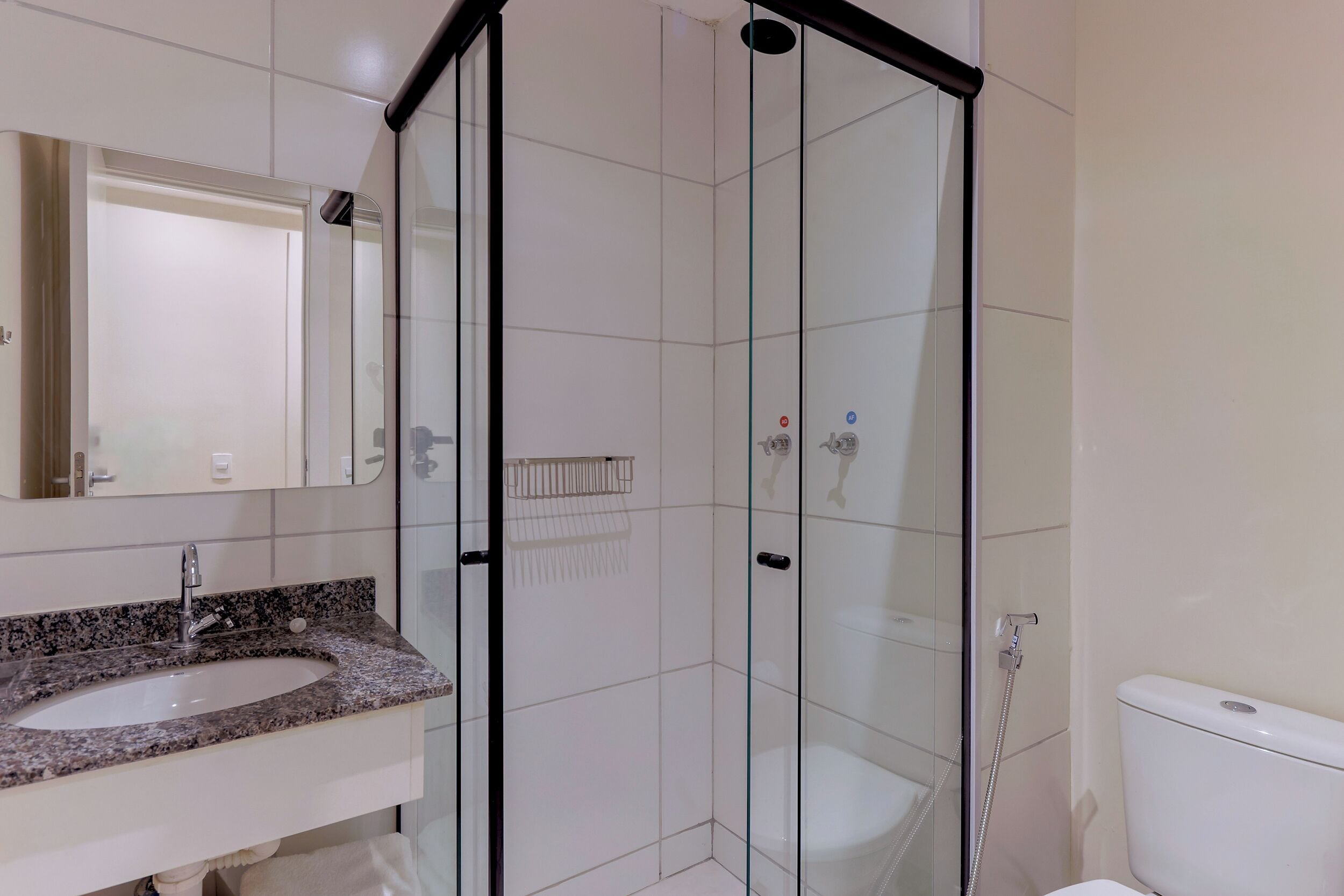 Ein Badezimmer mit einer gläsernen Duschkabine, einem Waschbecken mit Granitplatte und einer Toilette.