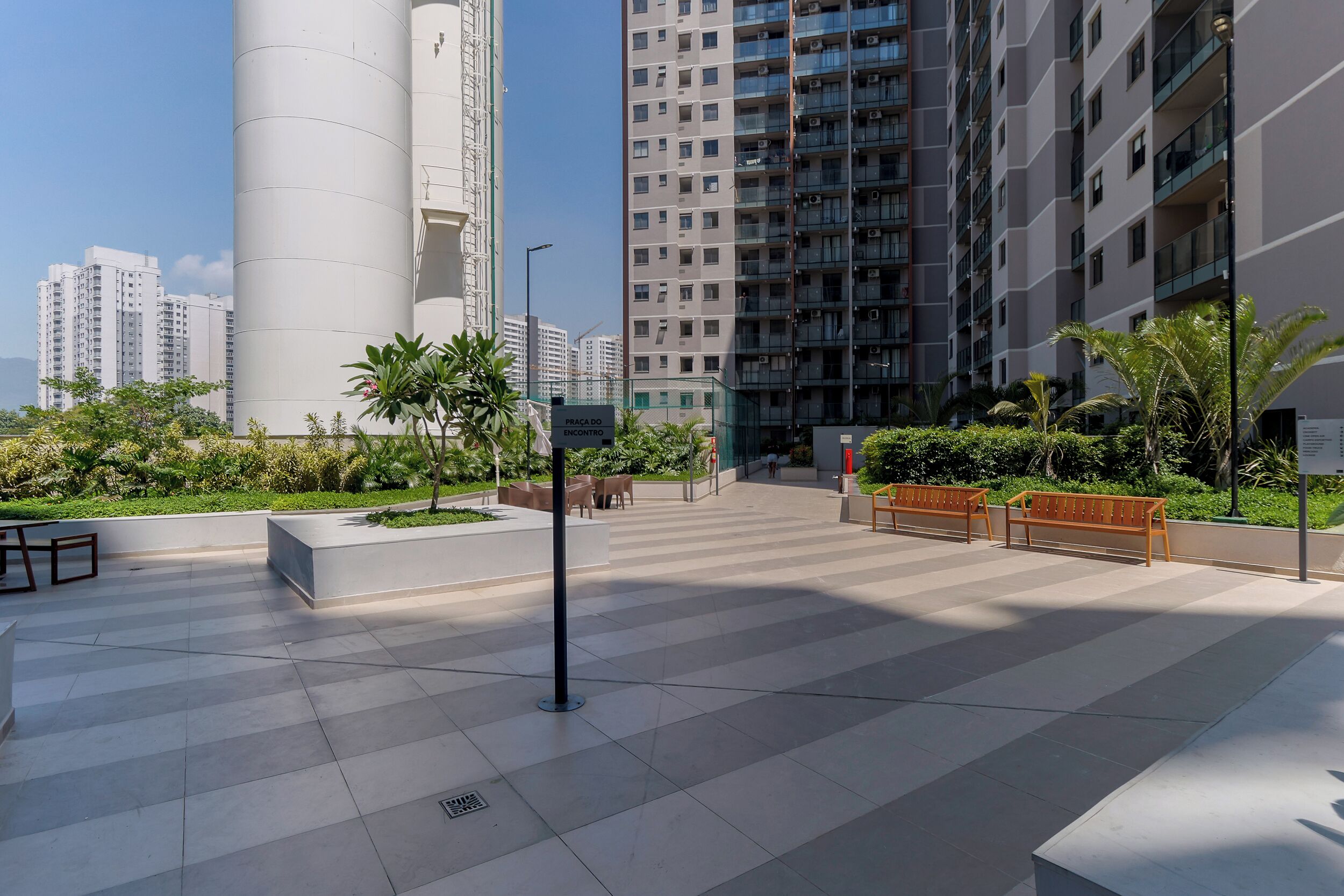 Una plaça urbana moderna amb zona d'estar, una estructura cilíndrica alta i edificis residencials al fons.