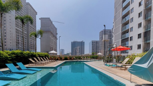 A swimming pool with lounge chairs and umbrellas, surrounded by high-rise buildings. - Charlie Rio Energy Porto Maravilha (Rio de Janeiro)