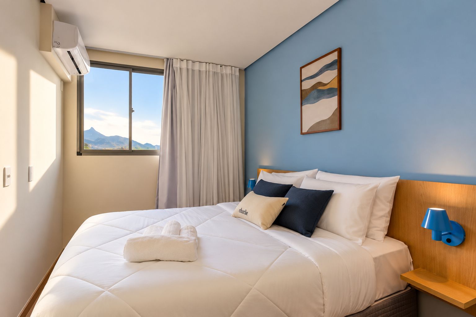 A hotel room with a bed, a window with curtains, a wall-mounted lamp, and a painting.