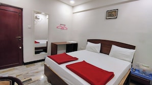 A hotel room with a bed, a bedside table, a mirror, a wardrobe, and a door. - Hotel Rayas (Kumbakonam)
