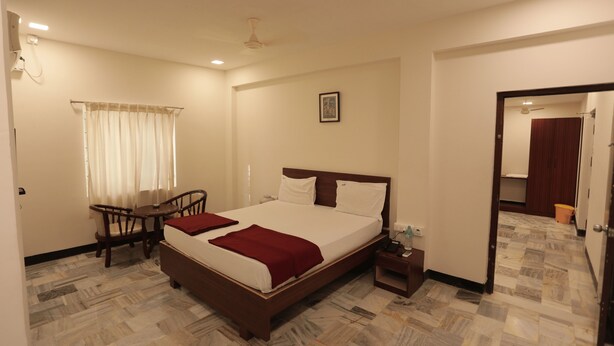 A hotel room with a bed, a desk, a chair, a nightstand, and a bathroom visible through an open door. - Hotel Rayas (Kumbakonam)
