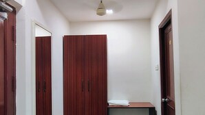 A hallway with a wooden wardrobe, a small table, a trash bin, and a blue mat. - Hotel Rayas (Kumbakonam)