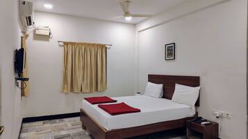 Quarto de hotel com cama, mesa de cabeceira, ventoinha no teto, ar condicionado, janela com cortinas e quadro na parede.