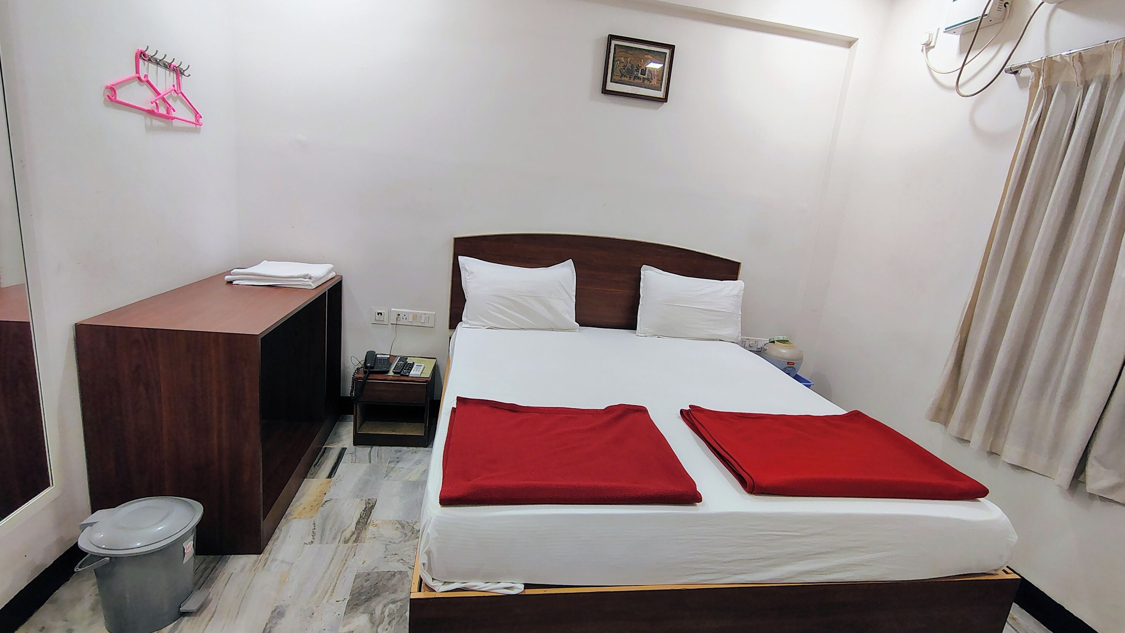 Habitació d'hotel amb llit, escriptori, telèfon, paperera i un quadre a la paret.