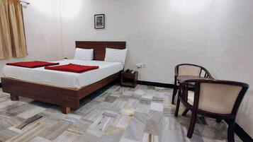 Habitación de hotel con cama de madera, ropa de cama blanca, una manta roja, una mesita de noche pequeña con un teléfono y una silla.