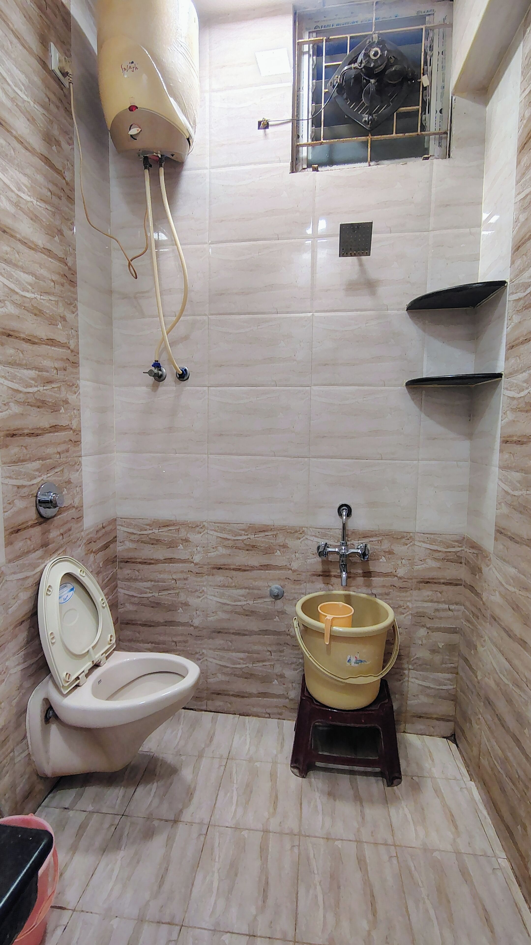 A bathroom with a toilet, a bidet, a water heater, and a bucket.