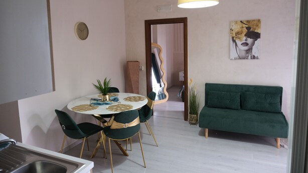 Un comedor con una mesa redonda, sillas, una lámpara colgante, un sofá, un reloj y un cuadro en la pared.