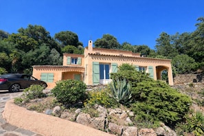 A Mediterranean-style villa with a tiled roof, a stone wall, and a garden with cacti and shrubs.