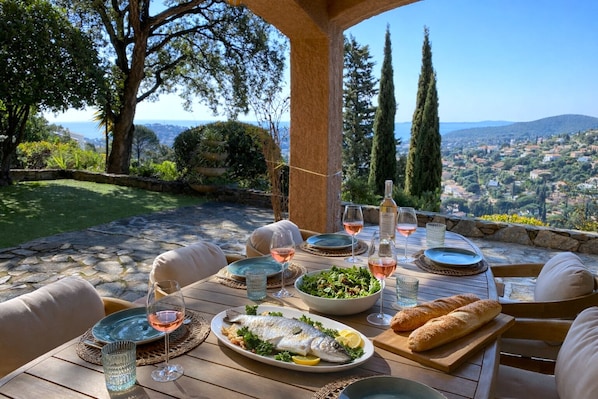 An outdoor dining area with a table set for a meal, surrounded by greenery and overlooking a scenic view.
