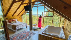 A spacious room with a large window, a bed, a sitting area, and a bathtub.