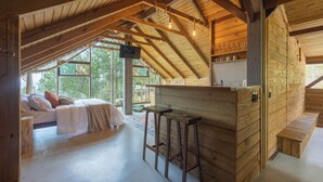 A wooden interior with a loft bedroom, a kitchen area, and a seating area with a view.