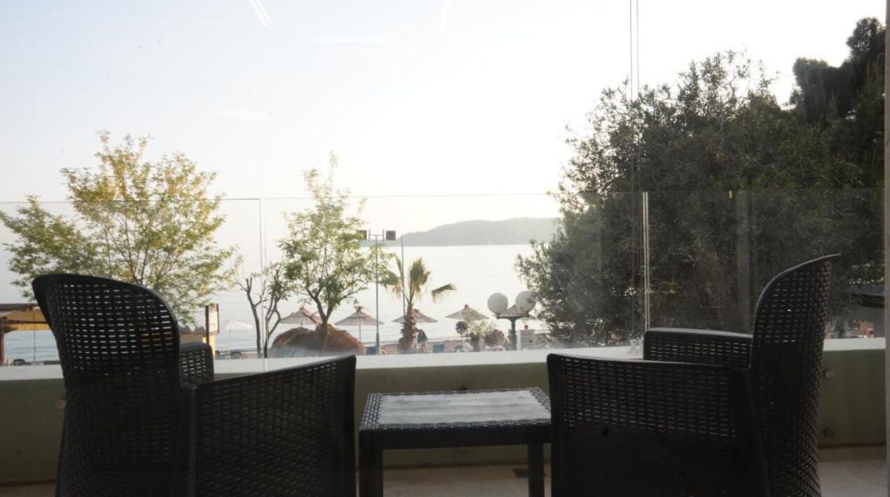 A balcony with wicker chairs and a table, overlooking a body of water and trees.