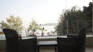 A balcony with wicker chairs and a table, overlooking a body of water and trees. - Modern, Bright Beachfront Flat in Rafailovici (Rafailovići, Opština Budvag, Apartment 2, Bečićka Plaza, 85310, Montenegro)