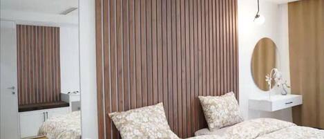 A modern bedroom with a large bed, a mirror, a bedside table, and a wooden panel wall.
