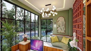 A modern living room with large windows, a flat-screen TV, a sofa, and decorative plants. - Palette Hotel Millennium City Centre (Gurugram)