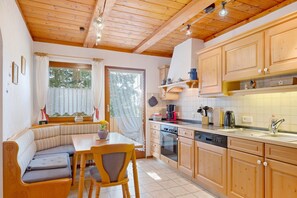 Eine gemütliche Küche mit Holzschränken, einem Essbereich mit einer Bank und einem Fenster mit Vorhängen.