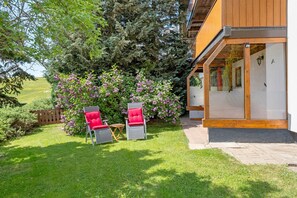 A wooden building with a covered patio area, two red chairs, and a small table. - Apartment Sommerruhe in Jostal near Titisee (Titisee-Neustadt)