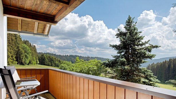 A balcony with wooden railings, two chairs, and a view of a forested landscape. - Apartment Sommerruhe in Jostal near Titisee (Titisee-Neustadt)