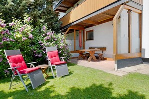 Een terras met twee rode stoelen, een houten tafel en een bank.