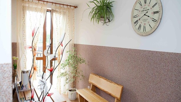 A room with a wooden bench, a wall-mounted clock, a potted plant, and a window with curtains.