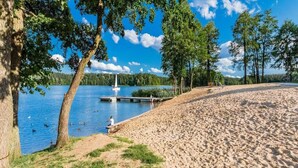 A sandy beach with a dock extending into a lake, surrounded by trees.