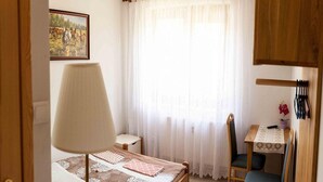 A bedroom with a bed, a desk, a chair, and a window with curtains.