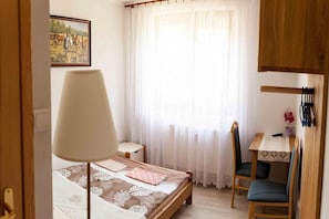 A bedroom with a bed, a desk, a chair, and a window with curtains.