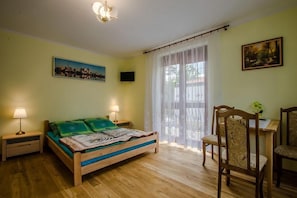 Ein Schlafzimmer mit Bett, Nachttischlampen, einem Sessel, einem Tisch, einem Bild und einem Fenster mit Vorhängen.