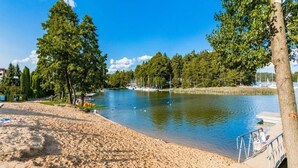 Una playa arenosa con un lago tranquilo, barcos y árboles.