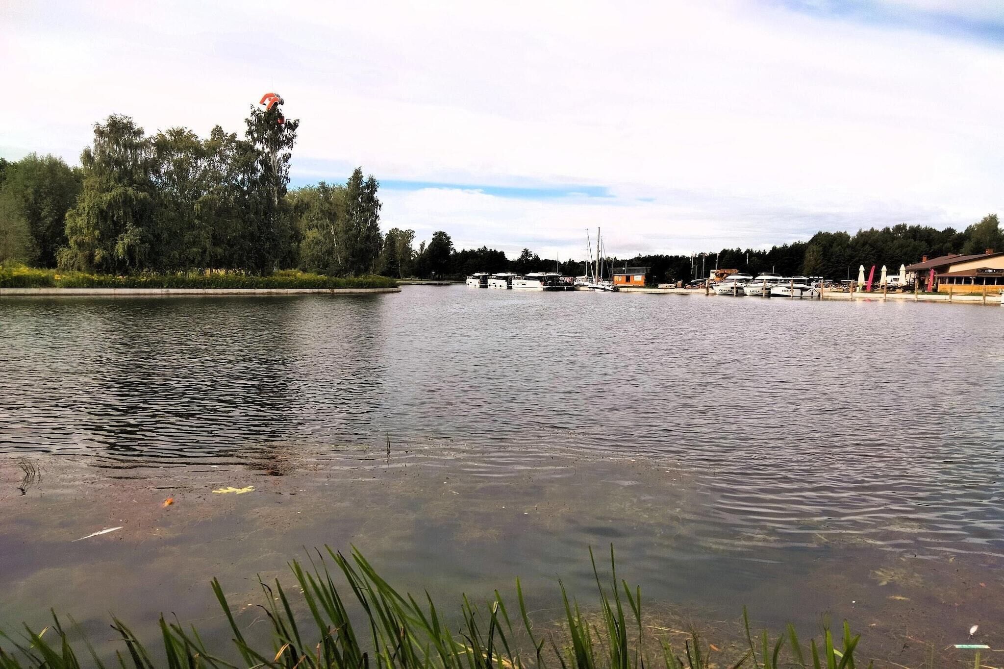 Un lago tranquilo con barcos amarrados en la orilla, rodeado de árboles y un edificio con techo inclinado.